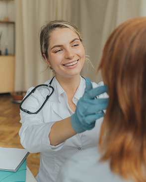 Eine Ärztin mit Stethoskop und blauen Handschuhen lächelt und spricht mit einer Patientin